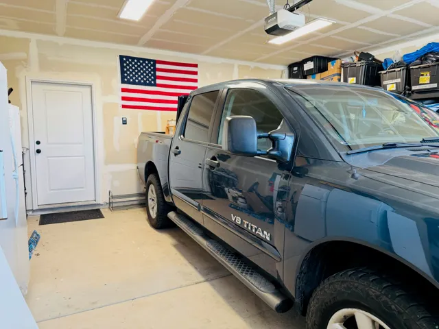 Attached garage with overhead lighting, a white panel door, and a garage door opener