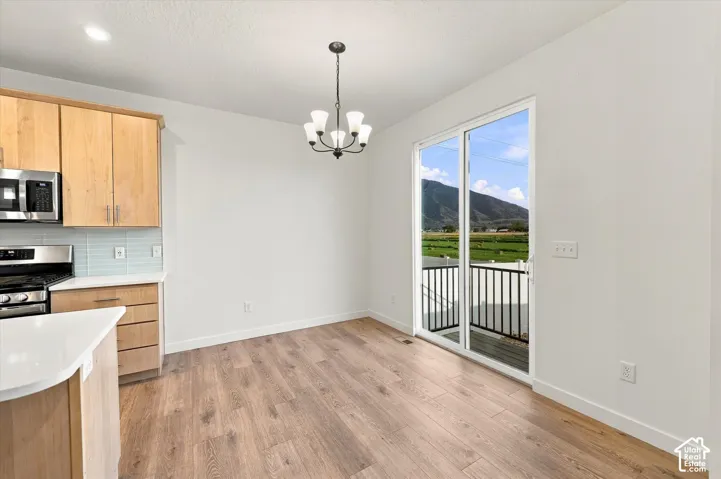 Wood-finish flooring, contemporary chandelier, kitchen cabinetry with stainless steel appliances, light blue tile backsplash, and sliding glass doors with balcony access