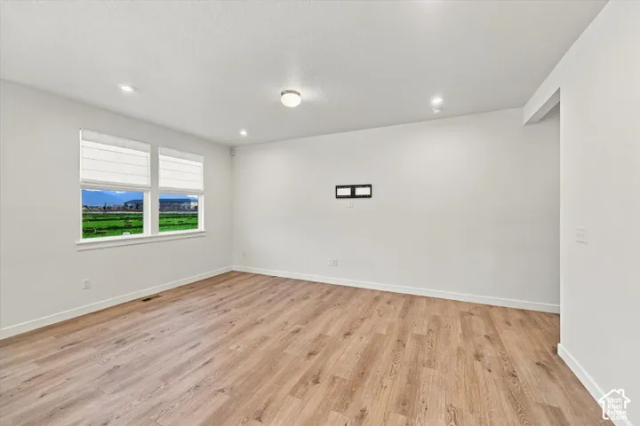 Wood-finish flooring throughout, recessed ceiling lighting, two windows with blinds, and a neutral wall color