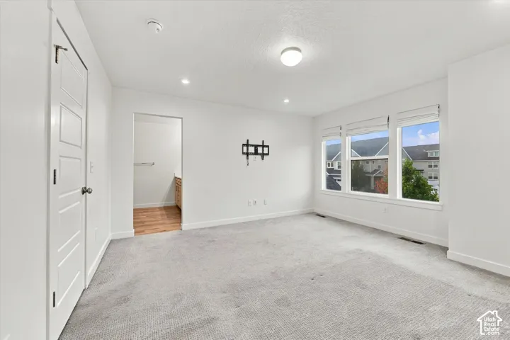 Neutral carpeted flooring, multiple recessed ceiling lights, and three large windows