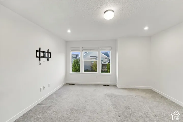 Recessed lighting, large triple window, wall-mounted television bracket, neutral carpeting, and a semi-flush mount ceiling light