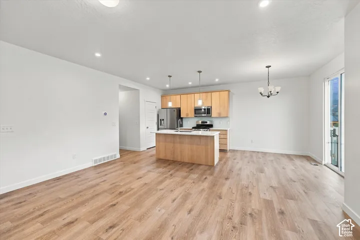 Open-concept living space featuring wood-finish flooring, recessed lighting, and a modern kitchen with a central island and stainless steel appliances