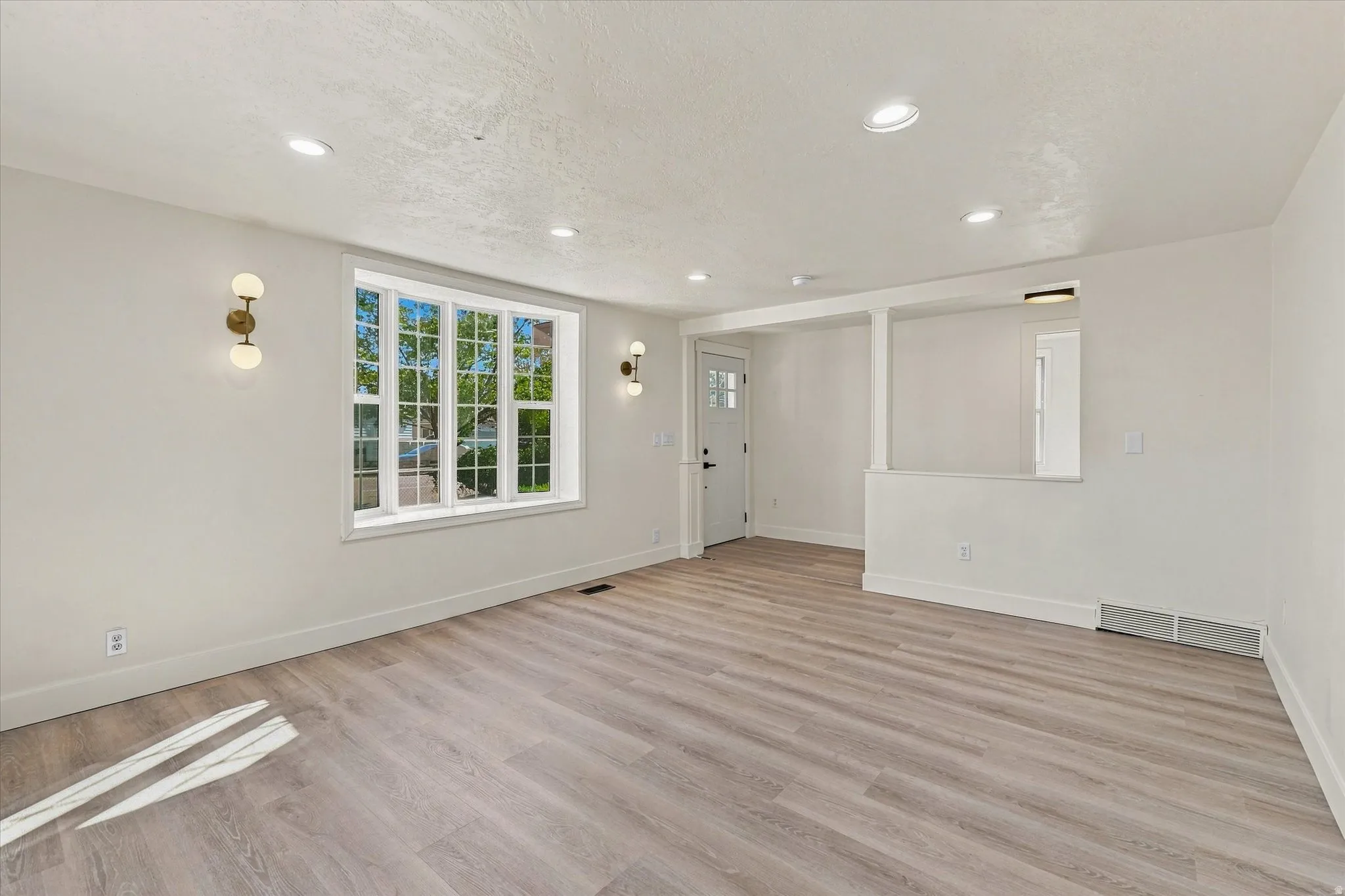 Recessed ceiling lighting, wood-finish flooring, bay window, modern wall sconces, and a paneled entry door