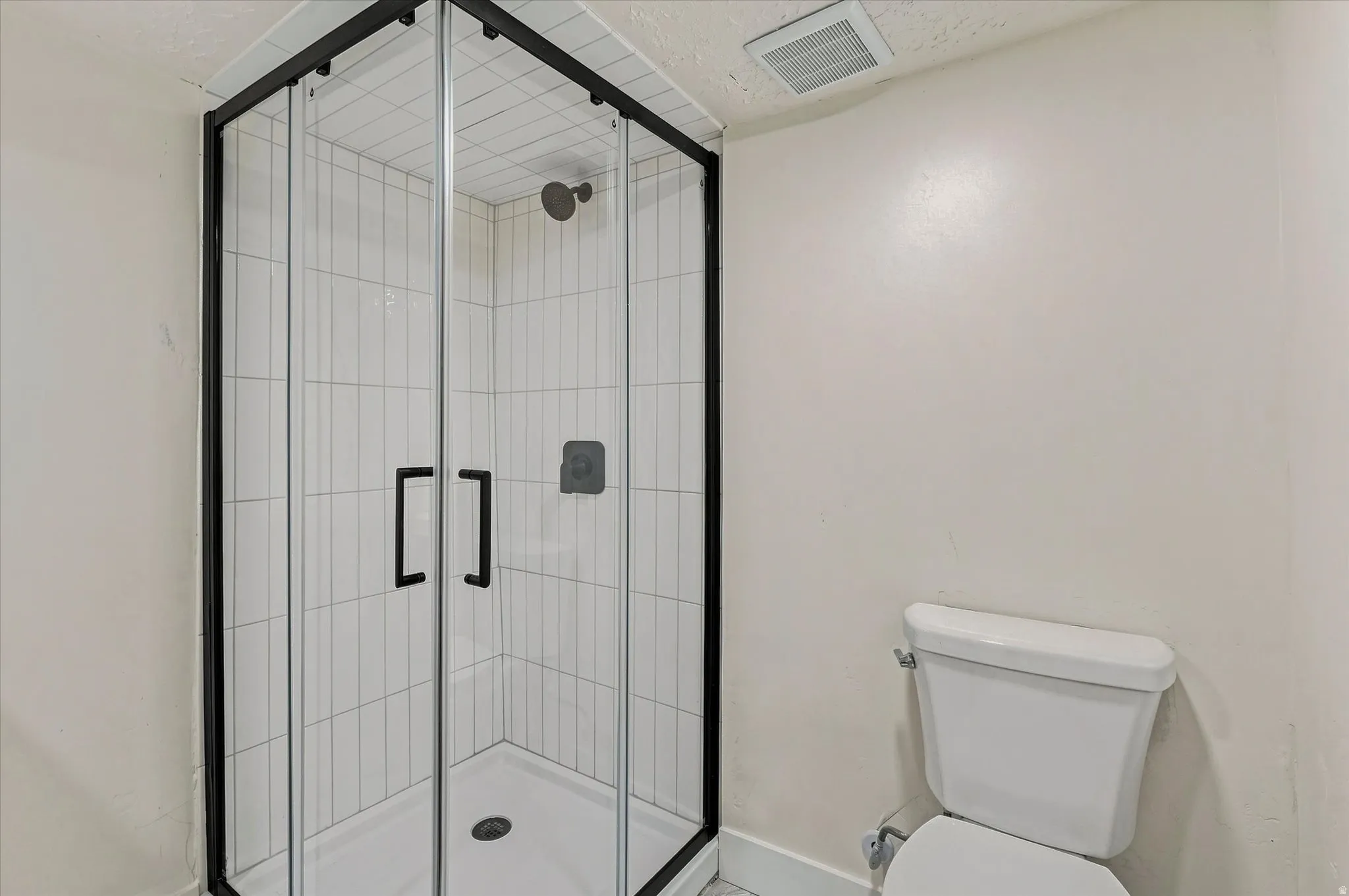 Corner glass shower enclosure with black framing, white subway tile surround, matte black shower fixtures, and a white toilet