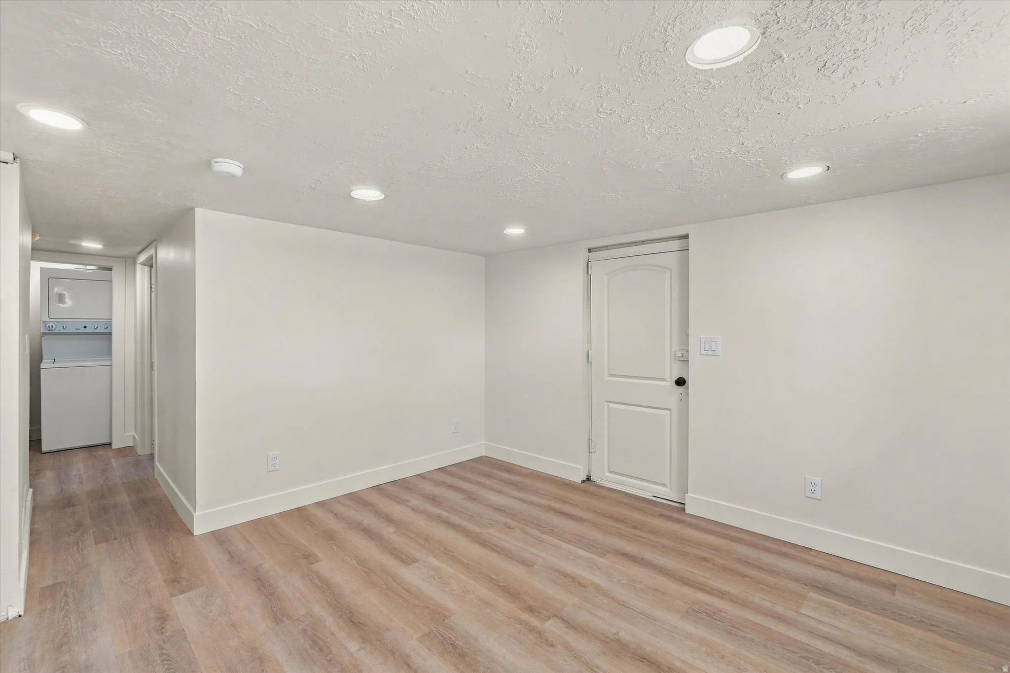 Recessed lighting illuminates the wood-finish flooring in this versatile space, featuring a built-in stacked washer and dryer