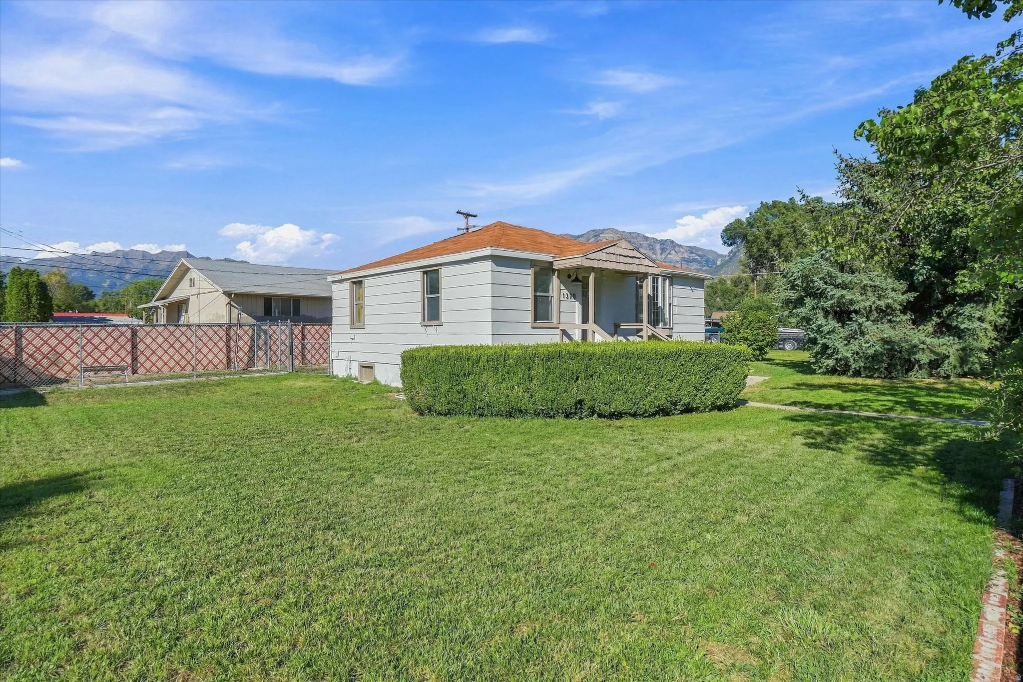 Expansive lawn with mature landscaping, fenced perimeter, and mountain backdrop