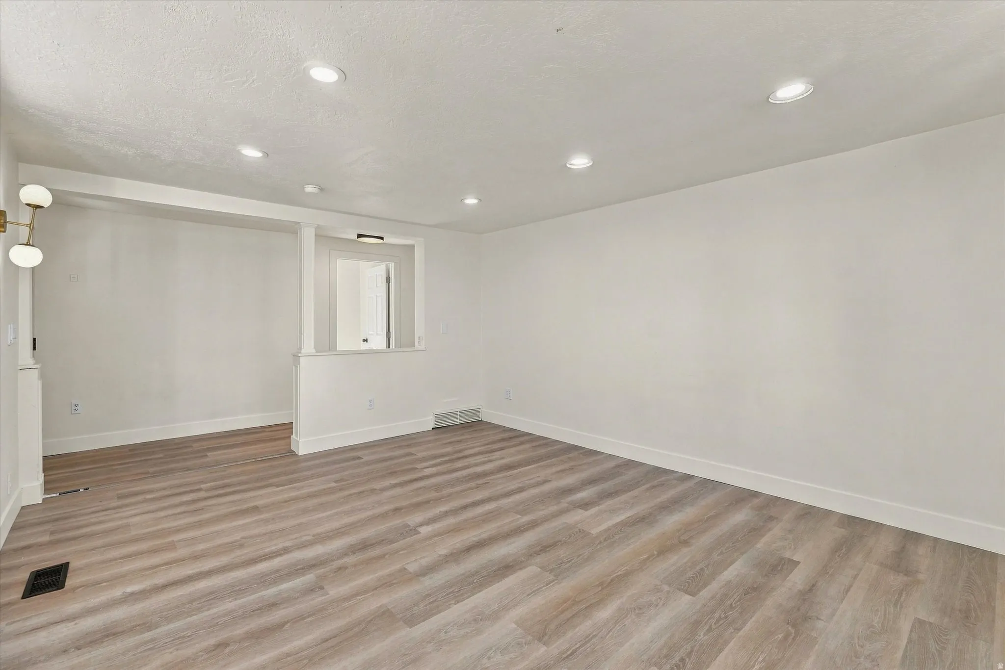 Spacious interior with wood-finish flooring, recessed lighting, and a modern wall-mounted fixture