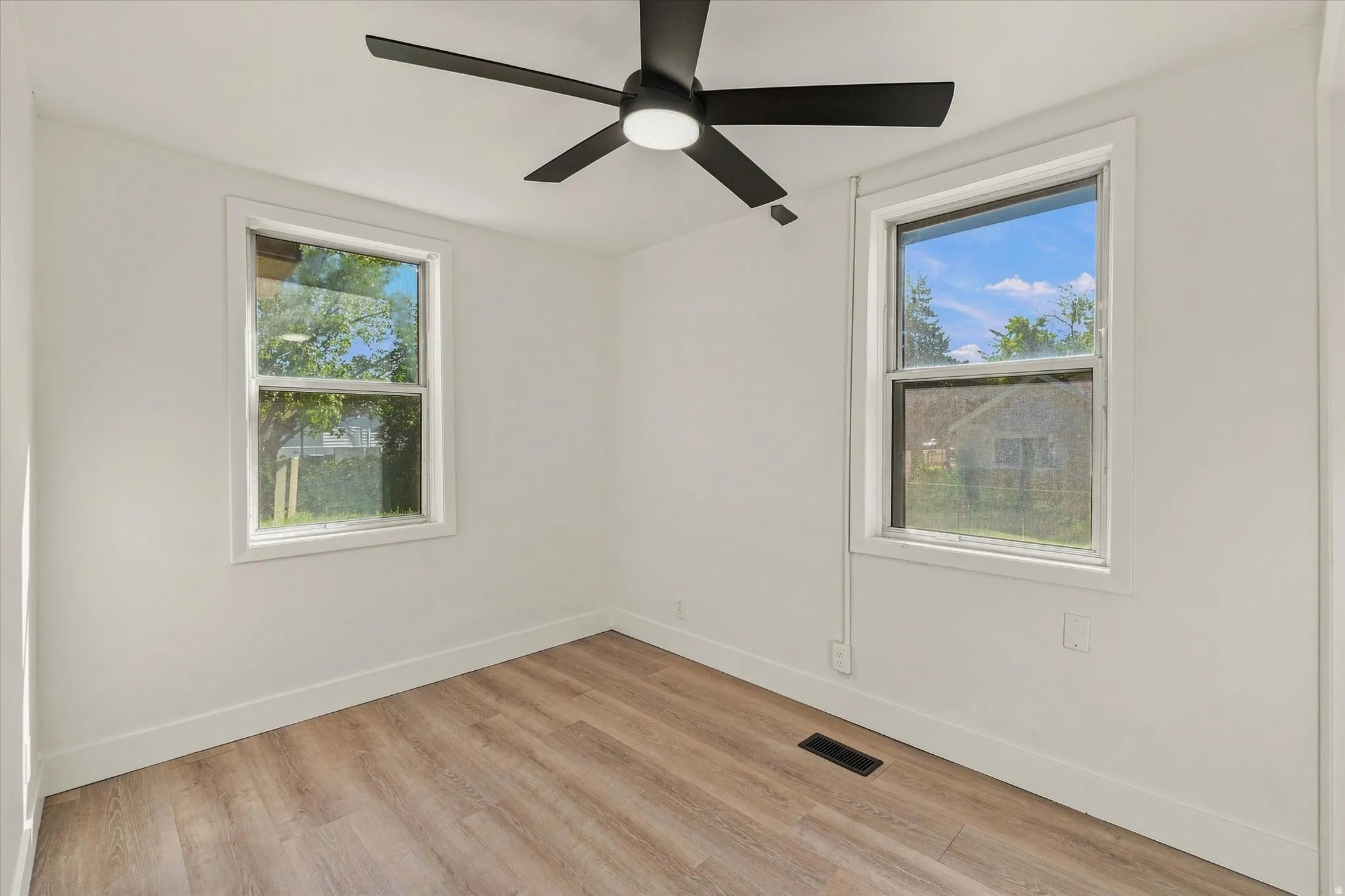 Crisp white walls with two windows, wood-finish flooring, and a ceiling fan with integrated lighting