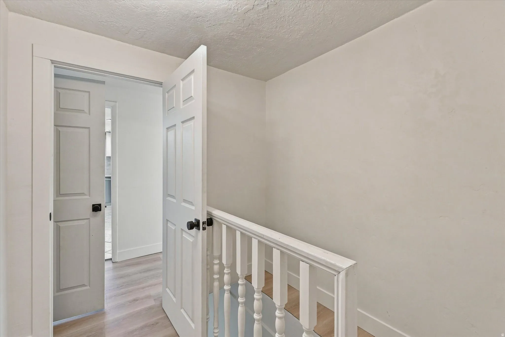 White paneled doors with matte black hardware, light wood-finish flooring, and a white wood-finish handrail
