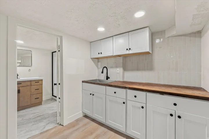 White shaker cabinetry with black hardware, wood-finish countertops, stainless steel sink with matte black faucet, and vertical tile backsplash