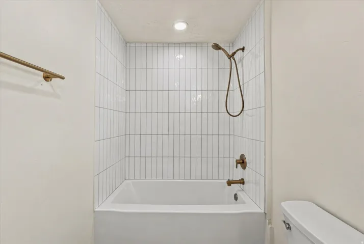 Bathtub with vertical white tile surround, a bronze shower head, and matching bronze fixtures