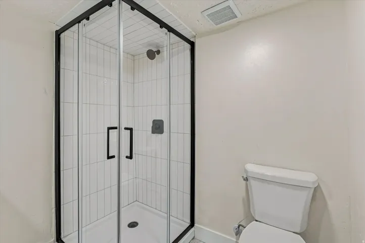 Corner glass shower enclosure with black framing, white subway tile surround, matte black shower fixtures, and a white toilet