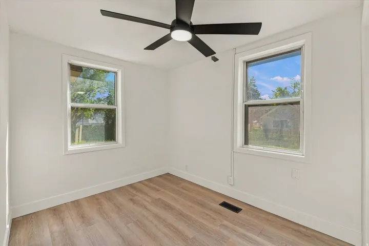 Crisp white walls with two windows, wood-finish flooring, and a ceiling fan with integrated lighting