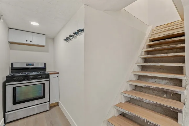 Stainless steel range with a built-in oven, overhead white cabinetry, and wood-finish flooring