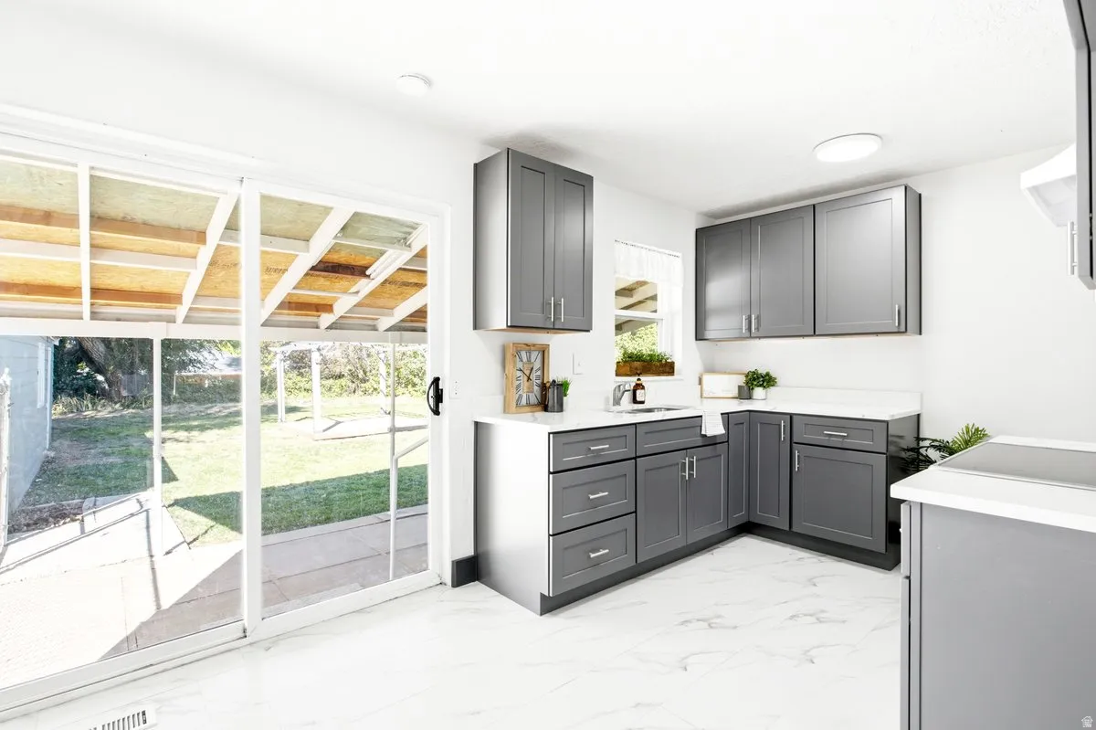 Kitchen featuring gray cabinetry, white countertops, stainless steel sink, tile flooring, and sliding glass doors to the patio