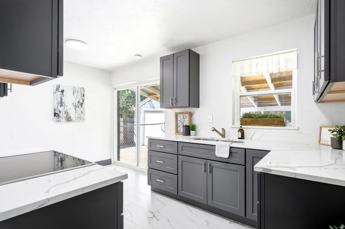 Kitchen featuring dark gray cabinetry, white countertops with veining, a stainless steel sink with a gooseneck faucet, white tiled flooring, and a sliding glass door