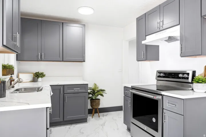 Kitchen featuring shaker-style cabinetry, stainless steel appliances, a range hood, quartz countertops, and a stainless steel sink