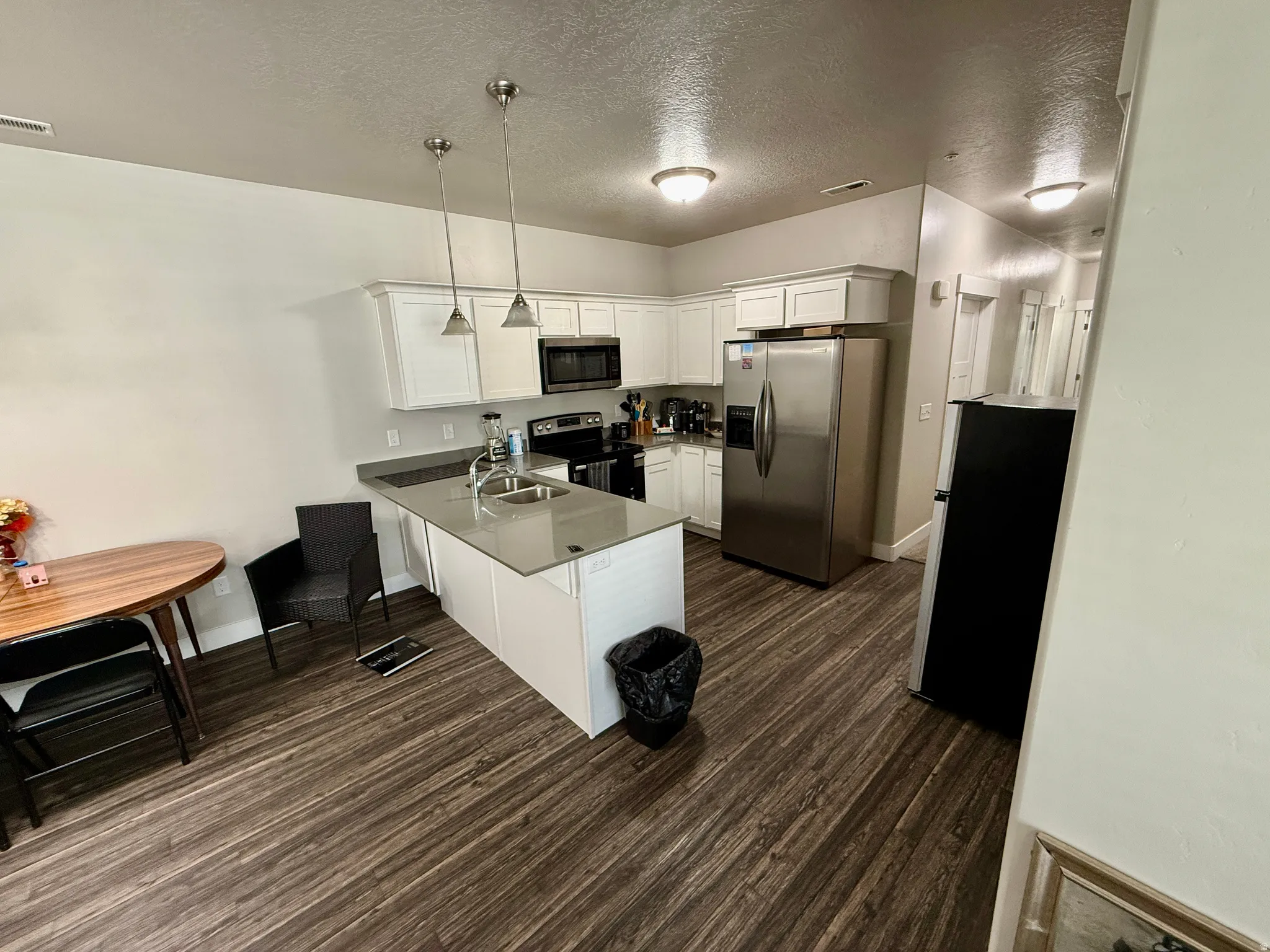Kitchen featuring wood-finish flooring, white cabinetry, a central island with a sink, and stainless steel appliances