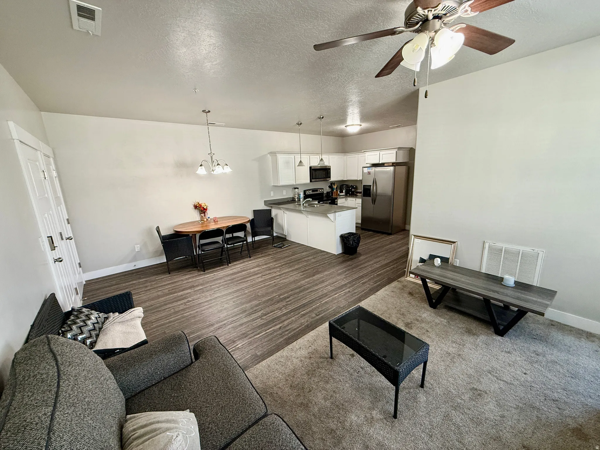 Open-concept living area featuring wood-finish flooring, white cabinetry, stainless steel appliances, and a ceiling fan with light fixture