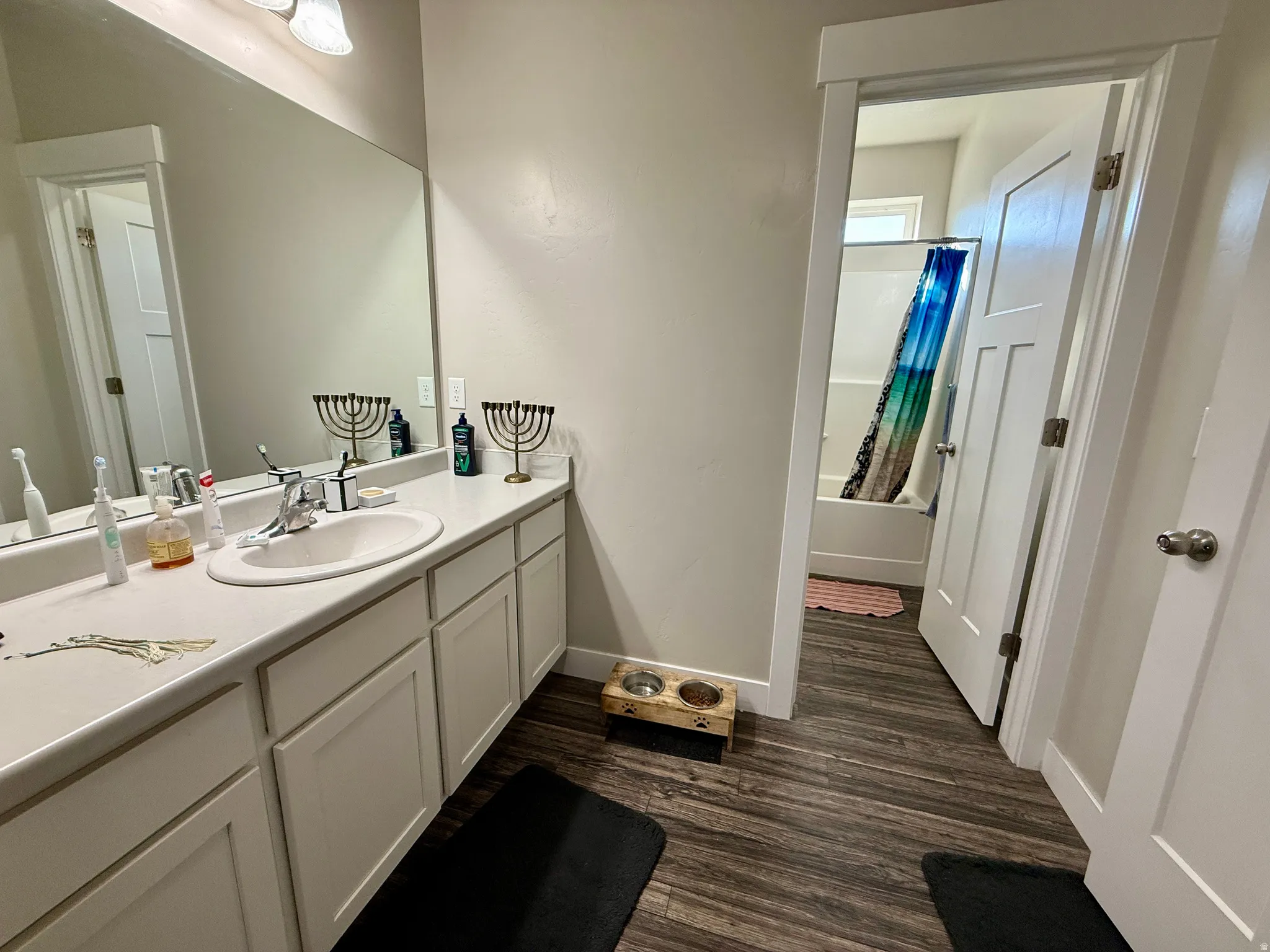 Vanity with an integrated sink, white cabinetry, a large wall-mounted mirror, and wood-finish flooring