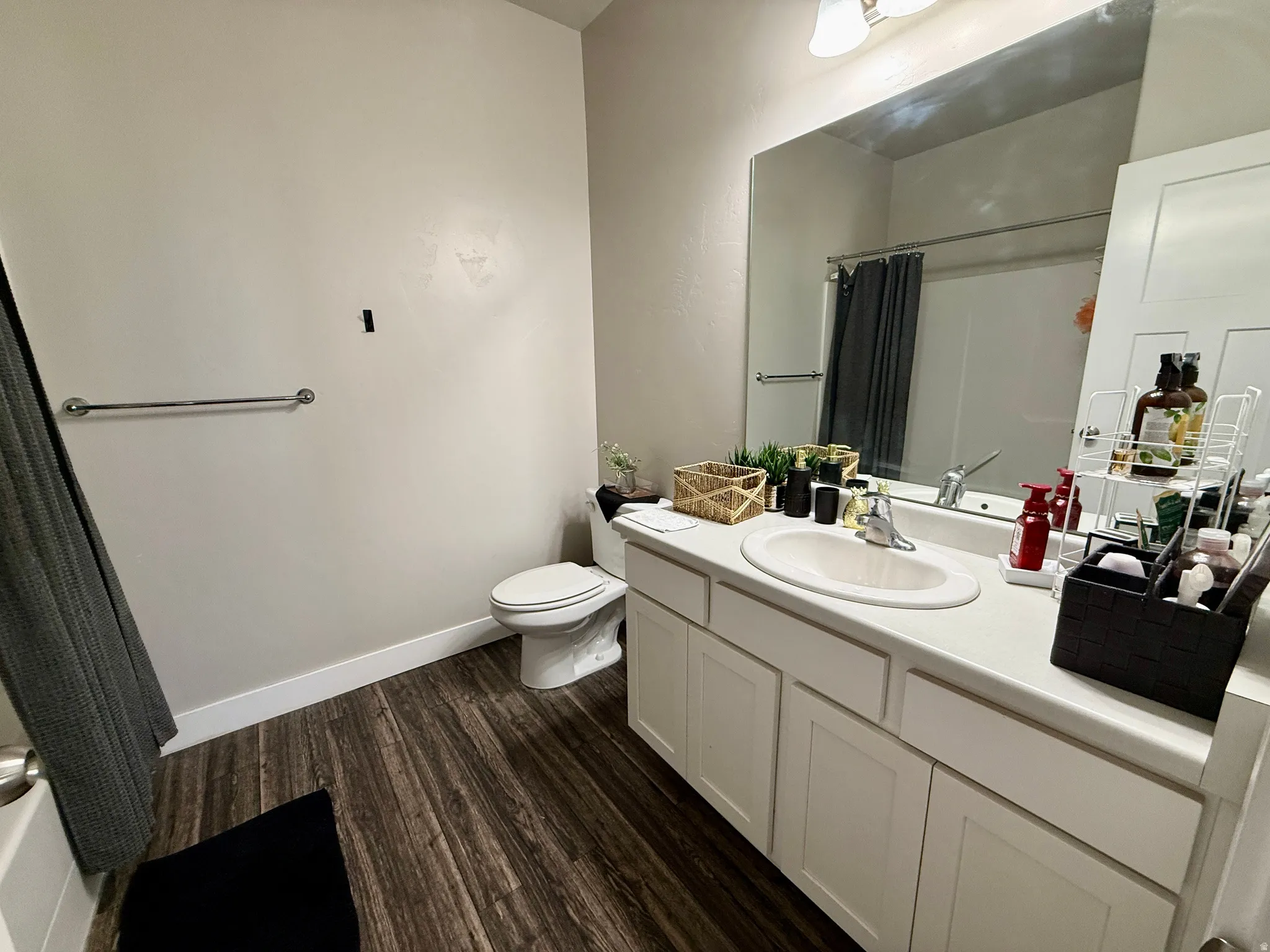 Modern vanity with an integrated sink and base cabinetry, wood-finish flooring, and a full-width mirror
