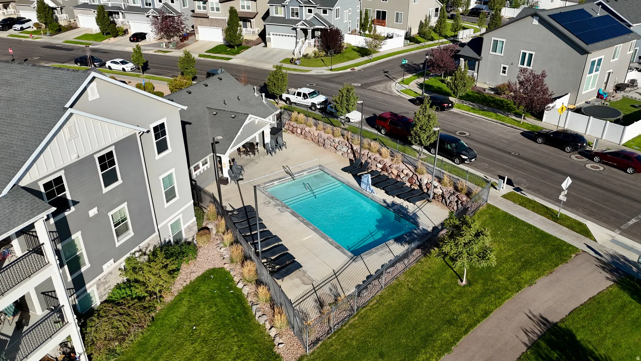 Community pool with surrounding lounge chairs, manicured green space, and paved walking path