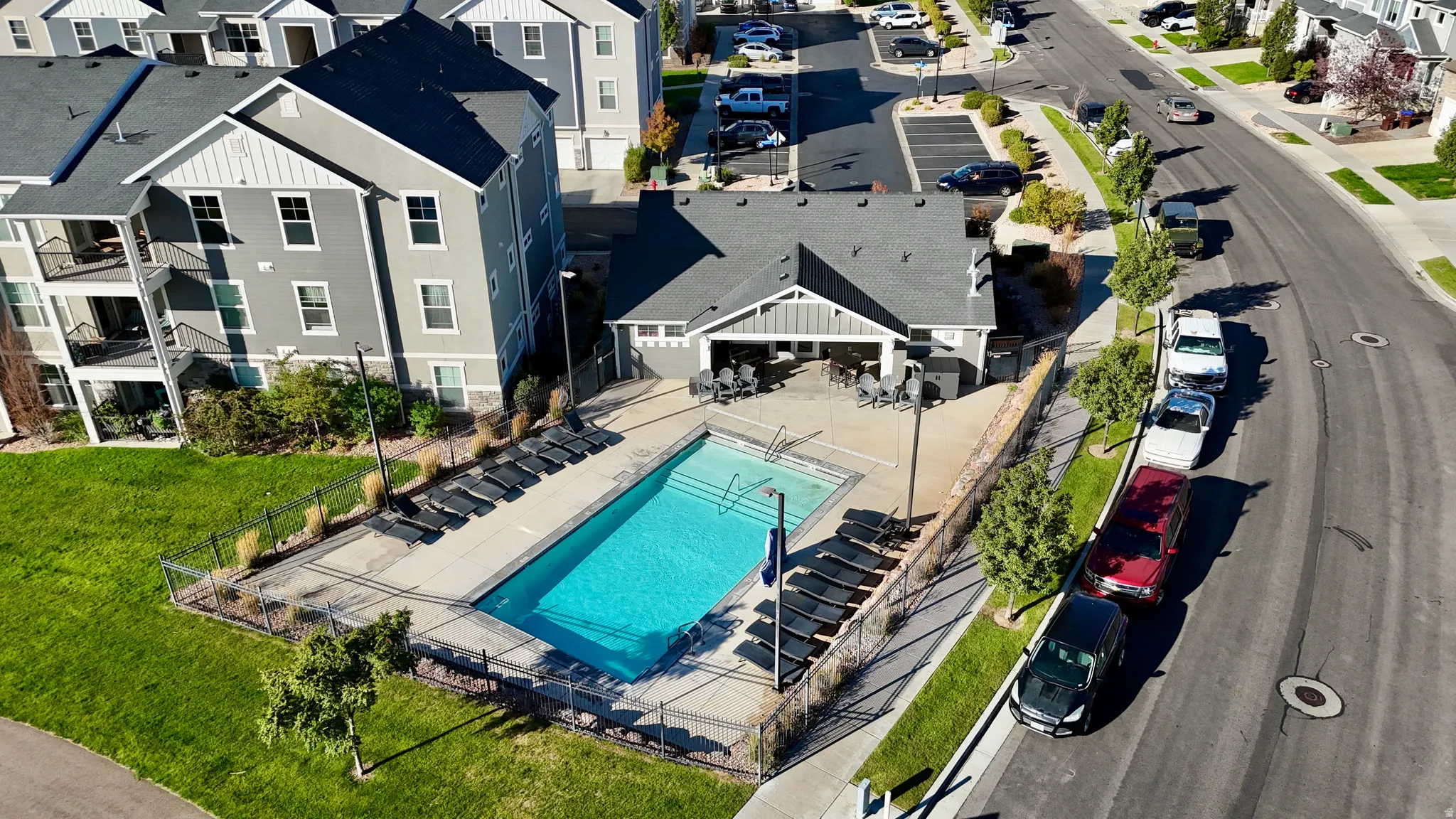 Community swimming pool with surrounding lounge seating, adjacent clubhouse building, and nearby residential structures