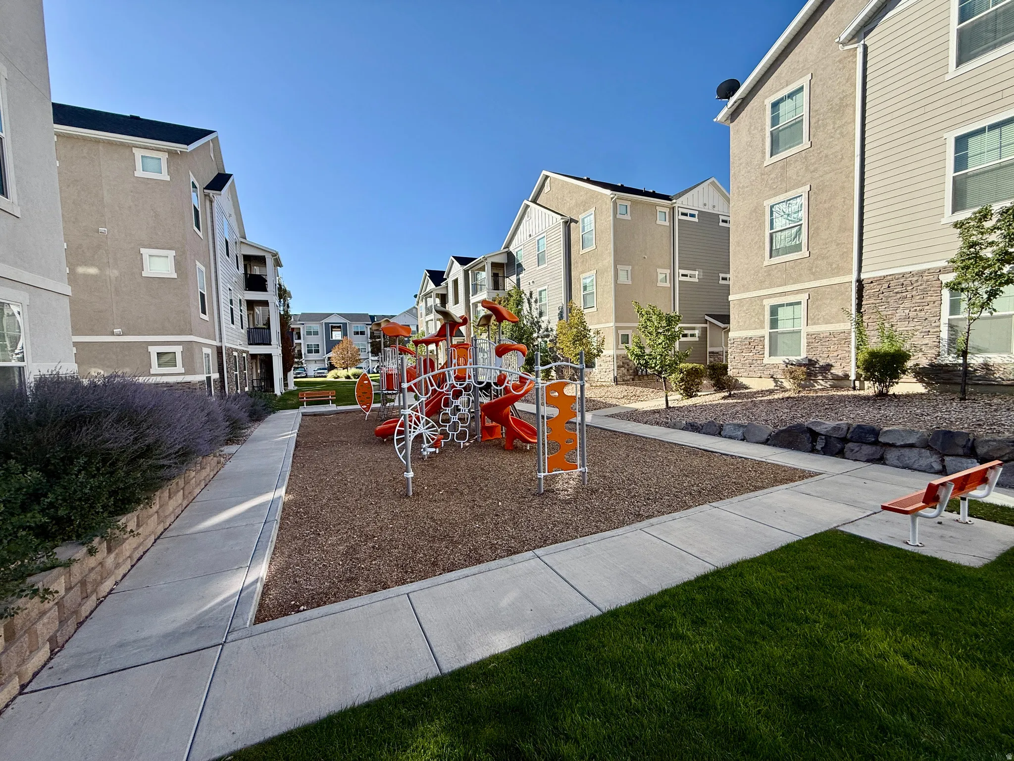 Outdoor playground with slides and climbing structures, surrounded by landscaped rock walls and manicured green spaces
