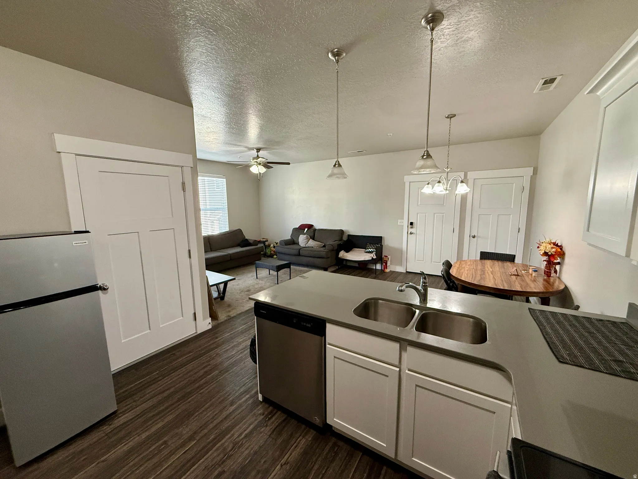 Open concept living area with wood-finish flooring, white paneled doors, and a kitchen island featuring a double stainless steel sink