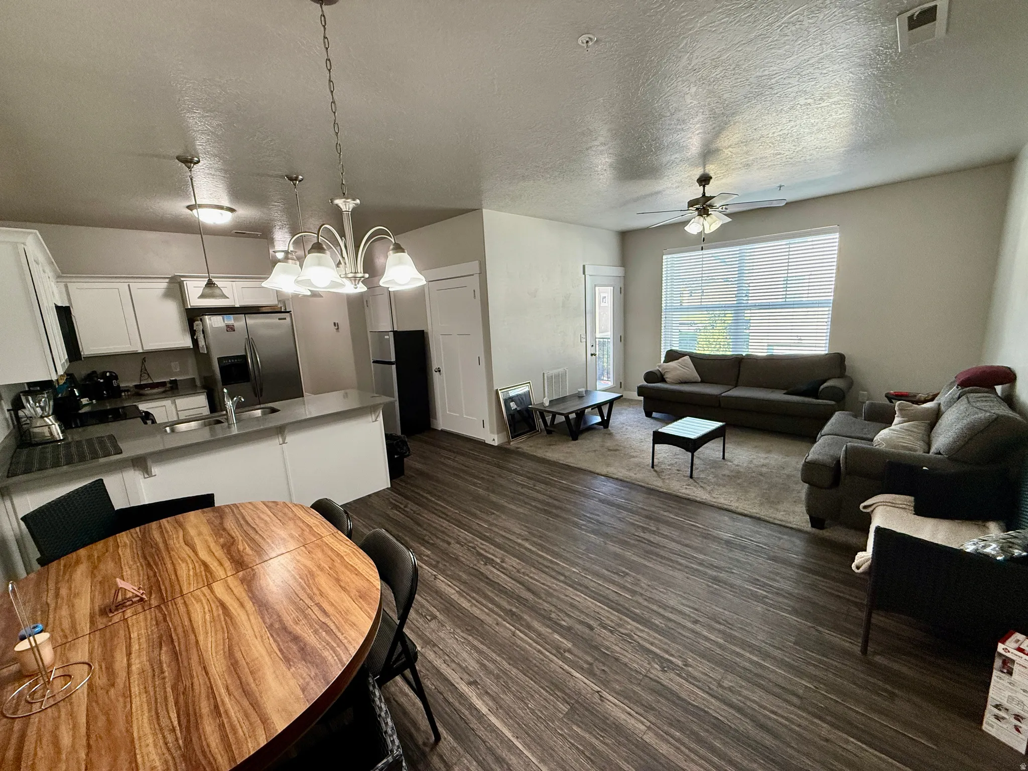 Open concept living area featuring wood-finish flooring, a ceiling fan, and a large window with blinds