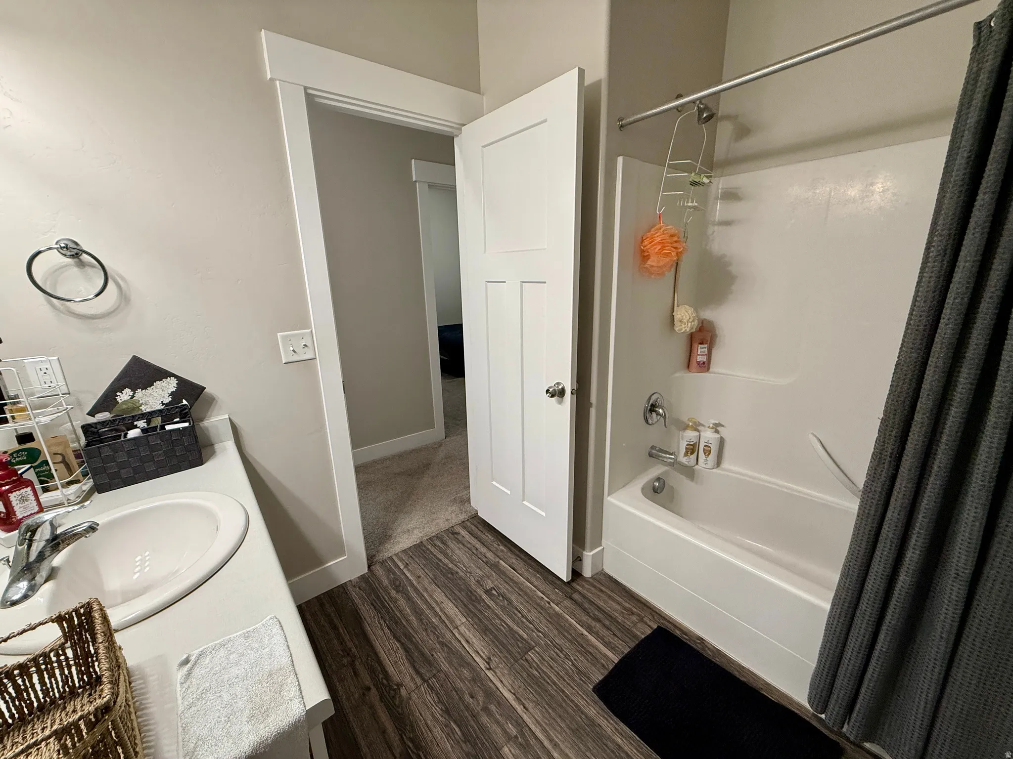 Bathroom featuring wood-finish flooring, a white vanity with an integrated sink, a chrome faucet, a towel ring, and a white tub/shower combination