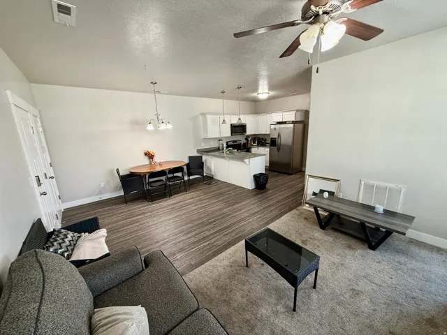Open-concept living area featuring wood-finish flooring, white cabinetry, stainless steel appliances, and a ceiling fan with light fixture
