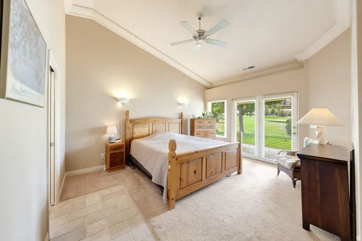 Vaulted ceiling with crown molding, double French doors, large windows, ceiling fan, and carpeted flooring with tile entry