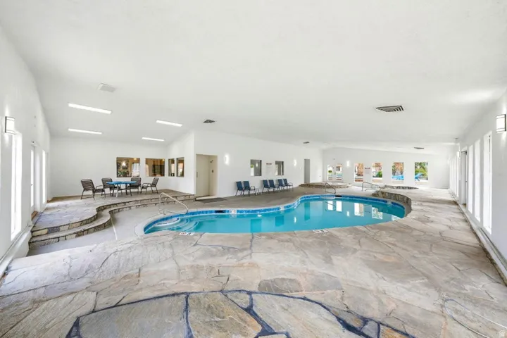 Indoor swimming pool with irregular flagstone decking, a built-in hot tub, and angled ceilings