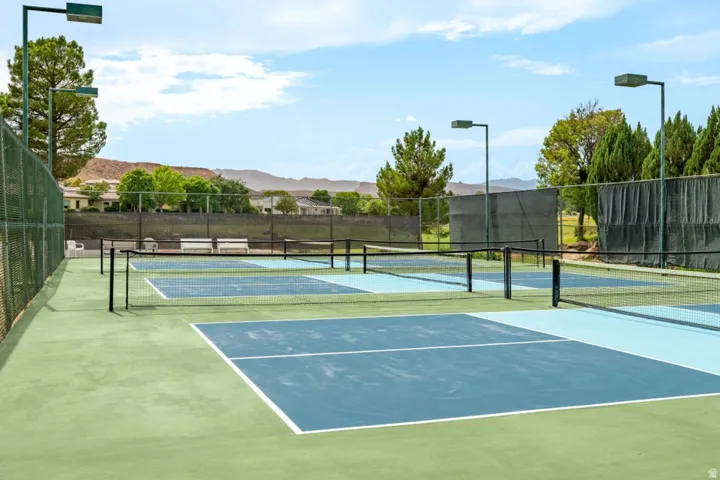 Multiple outdoor courts with green and blue playing surfaces, perimeter fencing, and overhead lighting