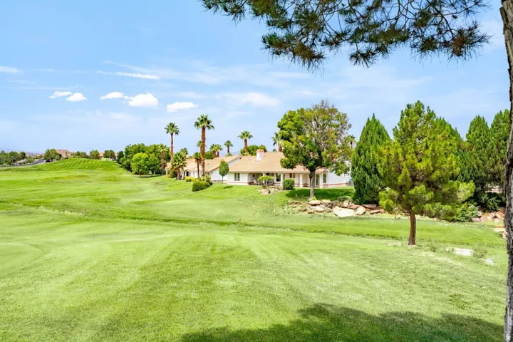 Expansive golf course property featuring mature trees, landscaped grounds, and a single-story residence with a light-colored exterior and a tiled roof