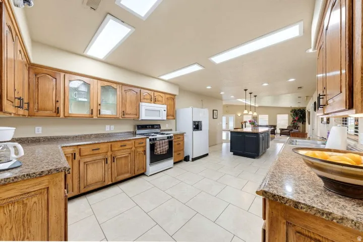 Kitchen featuring wood cabinetry, granite-style countertops, an island with pendant lighting, white appliances, and tile flooring