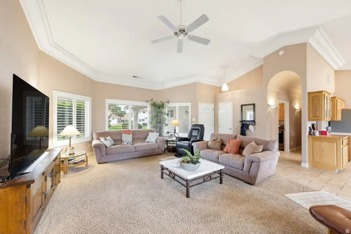 Vaulted ceiling with crown molding, ceiling fan, arched doorway, and built-in cabinetry