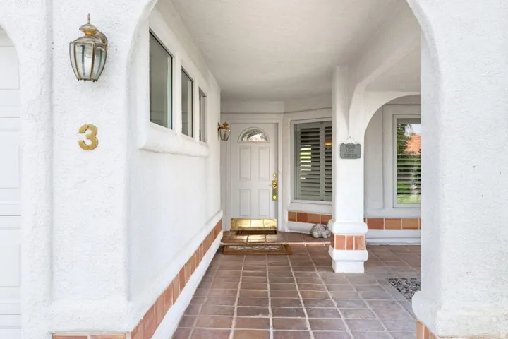 Arched entry with a brass sconce, terracotta tile flooring, and white stucco walls