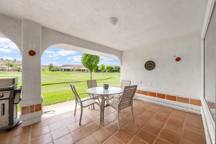 Covered patio with terracotta-style tile flooring, white stucco walls, and arched openings leading to a manicured lawn