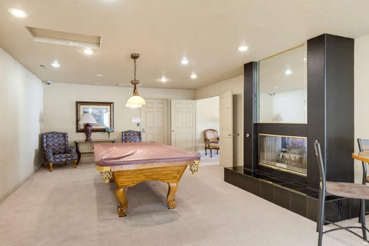 Recessed lighting throughout, accent pendant light fixture, built-in fireplace with black tile surround, and neutral carpeting