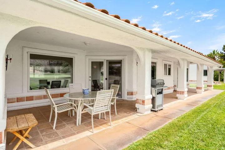 Covered patio featuring a tiled floor, white stucco columns with brick accents, and a red tile roof