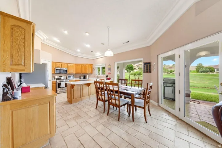 Kitchen featuring light wood cabinetry, stainless steel appliances, a center island with bar seating, tile flooring, and French doors leading to a patio
