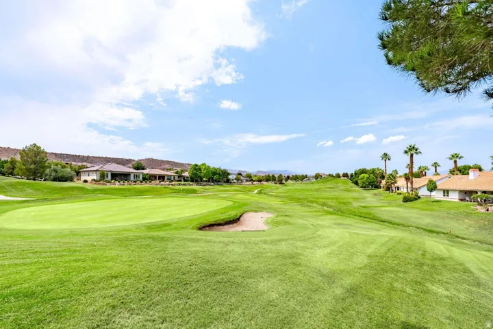 Expansive golf course featuring a green, sand trap, and distant residential structures