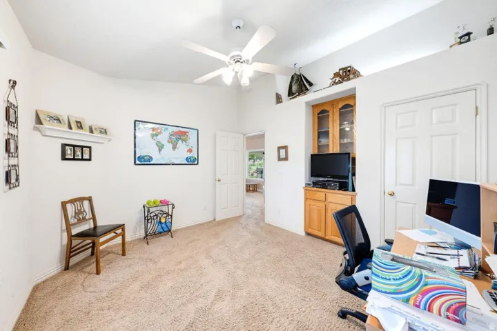 Vaulted ceiling with a ceiling fan, built-in cabinetry with glass doors, and carpeting