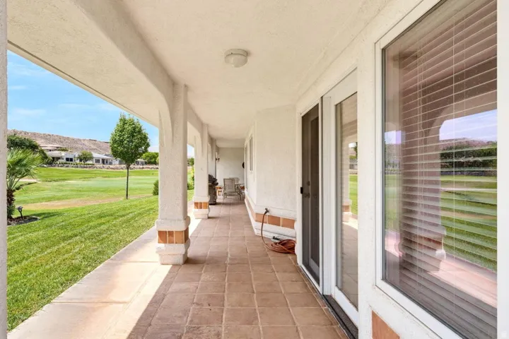 Covered patio with a tiled floor, multiple support columns, and an expansive lawn