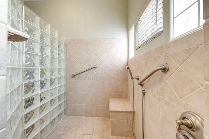 Tiled shower with glass block wall, built-in bench, handheld shower fixture, and grab bars