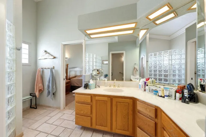 Expansive vanity featuring dual sinks, wood cabinetry, and a large mirror with integrated lighting