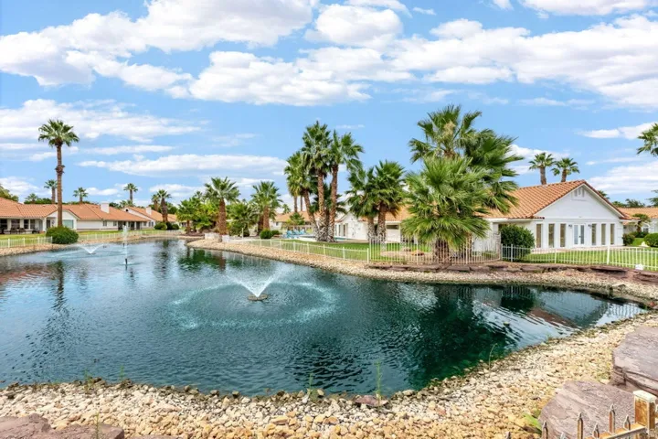 Water feature with multiple fountains, surrounded by mature palm trees, residential structures with tile roofs, and manicured lawns