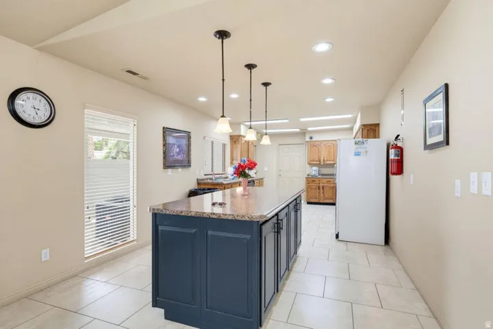Kitchen featuring a central island with a stone-finish countertop, pendant lighting, recessed lighting, tile flooring, and wood-finish cabinetry